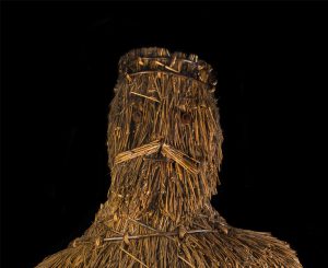 The face of King Alfred, a staw sculpture, against a black background.