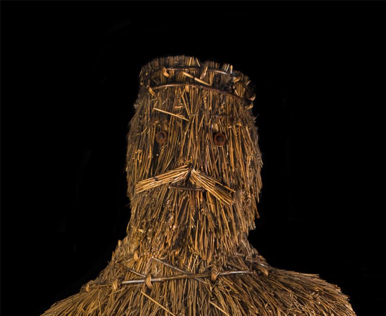 The face of King Alfred, a staw sculpture, against a black background.