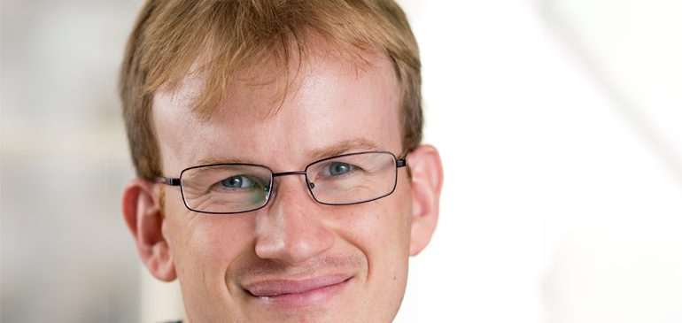 The head and shoulders of James Grande looking at the camera against a white background. He has short, ginger hair and glasses. He is smiling.