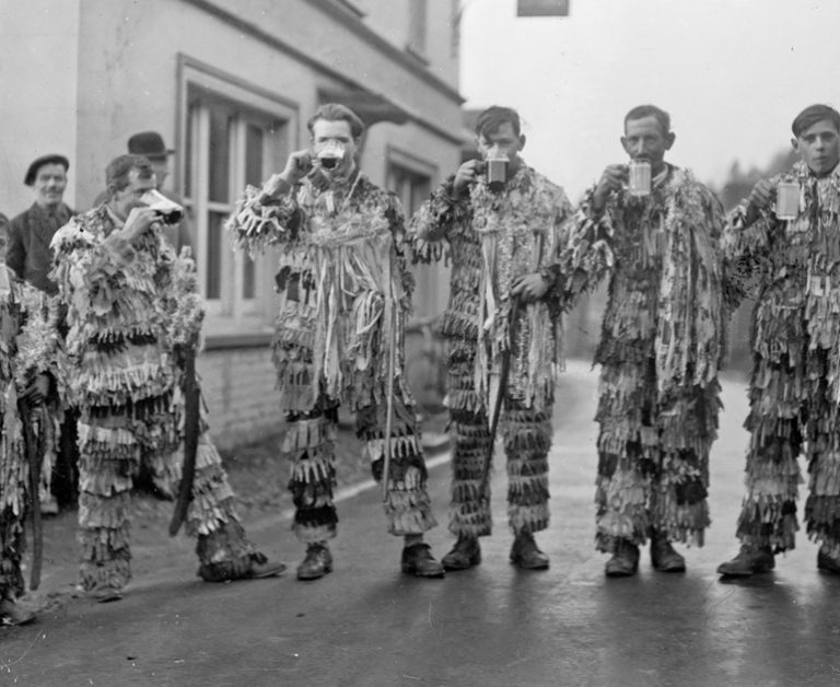 Black and white photograph of men dressed as mummers drinking pints