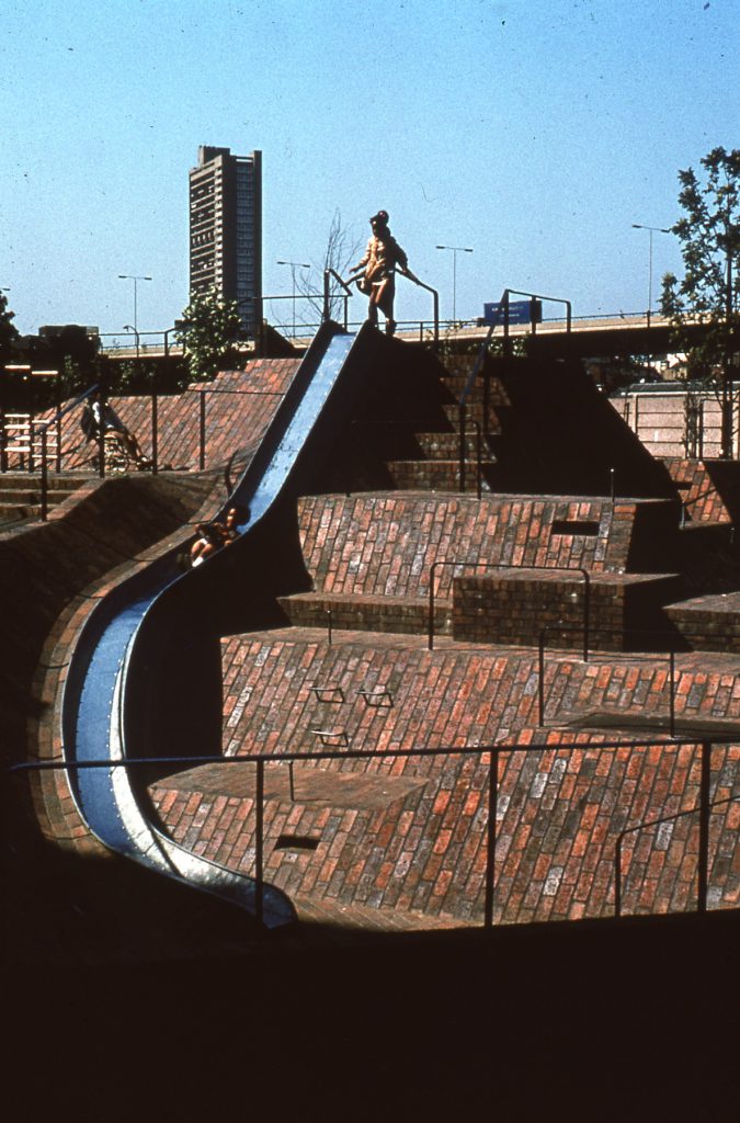 A colour photograph of children playing on a slide in the Brunel Estate, London.