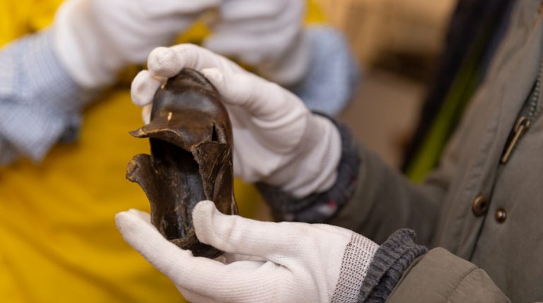 Hands in white gloves handling a small leather shoe from the MERL object collection