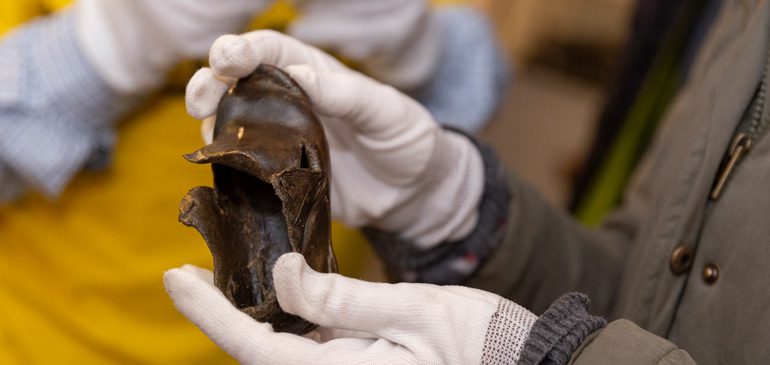 Hands in white gloves handling a small leather shoe from the MERL object collection