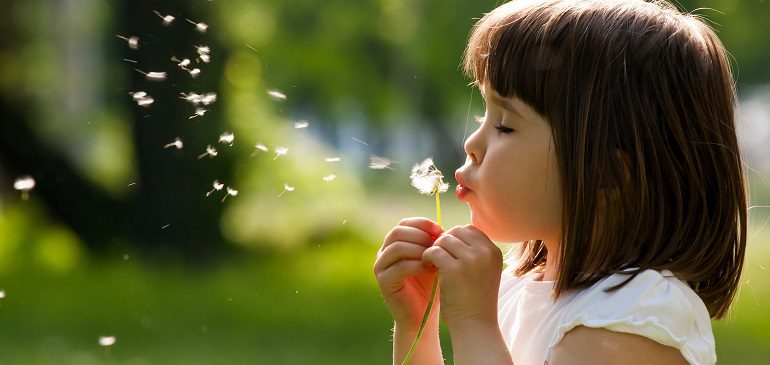 Profile of a girl blowing seeds off of a dandelion