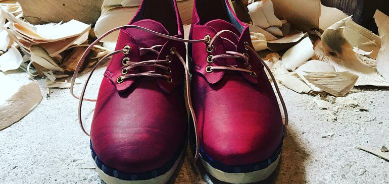 New pair of dark pink leather lace-up clogs with wood shavings in the background