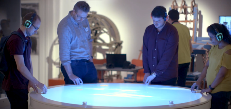 Four people standing around the interactive table in the OCL gallery