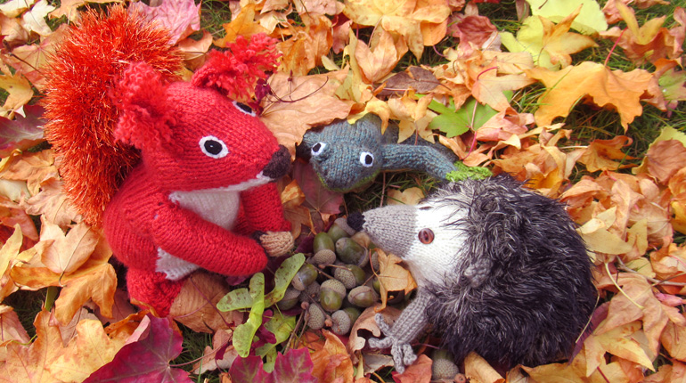 Knitted hedgehog poking its face out from a bed of colourful leaves for Autumnal Animals event