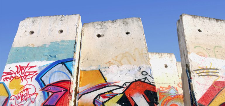 A section of the Berlin Wall with brightly coloured graffiti against a blue sky for the Popular Protest event