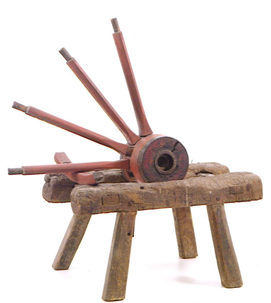 Large wooden trestle with four legs, with the top shaped to support a wagon wheel.
