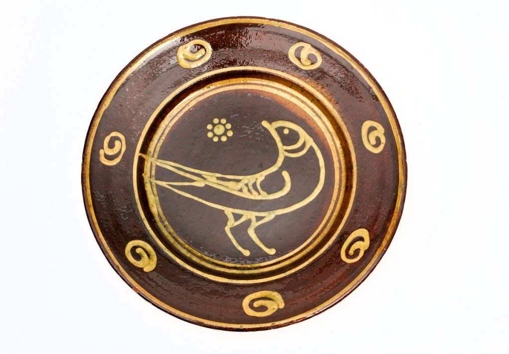 The large round dish is brown with a trailed slip design in yellow, which includes a bird in the centre