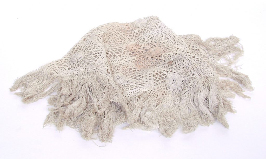 An antimacasser, a square lace cover with a tassled edge used for protecting seating material. It has yellow embroidery on cream linen.