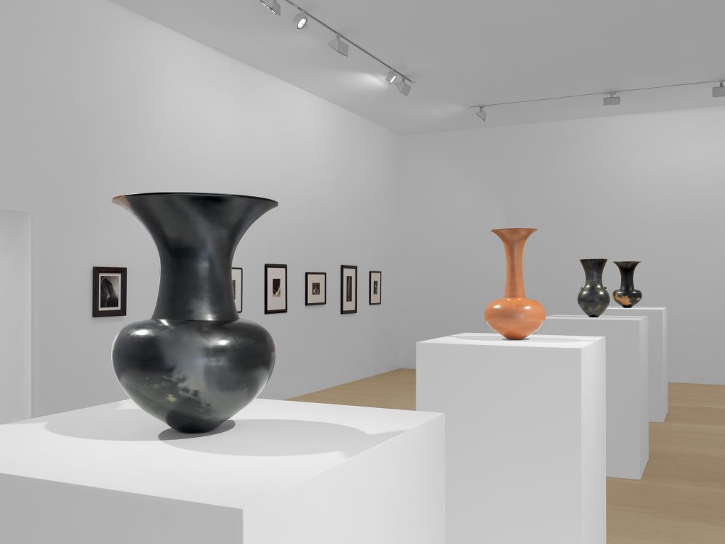Four pots on plinths. Three of the pots are predominantly black and one is orange