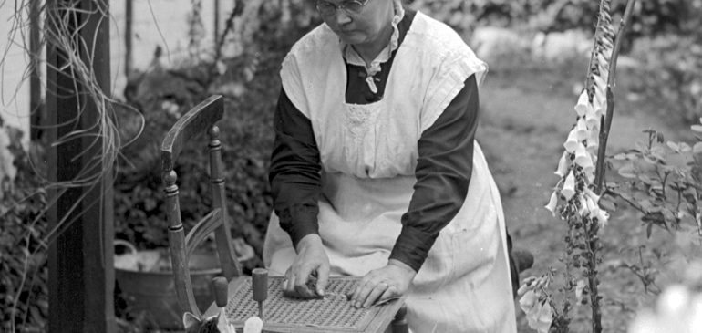 Woman caning a chair in garden with cat.