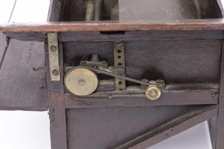 Detail of a small dark wooden threshing machine mechanism with cogs and workings visible.