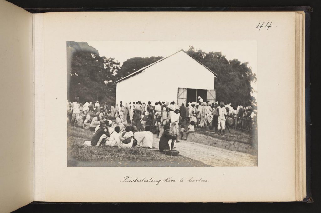Black and white image showing Indian workers outside a distribution hut.