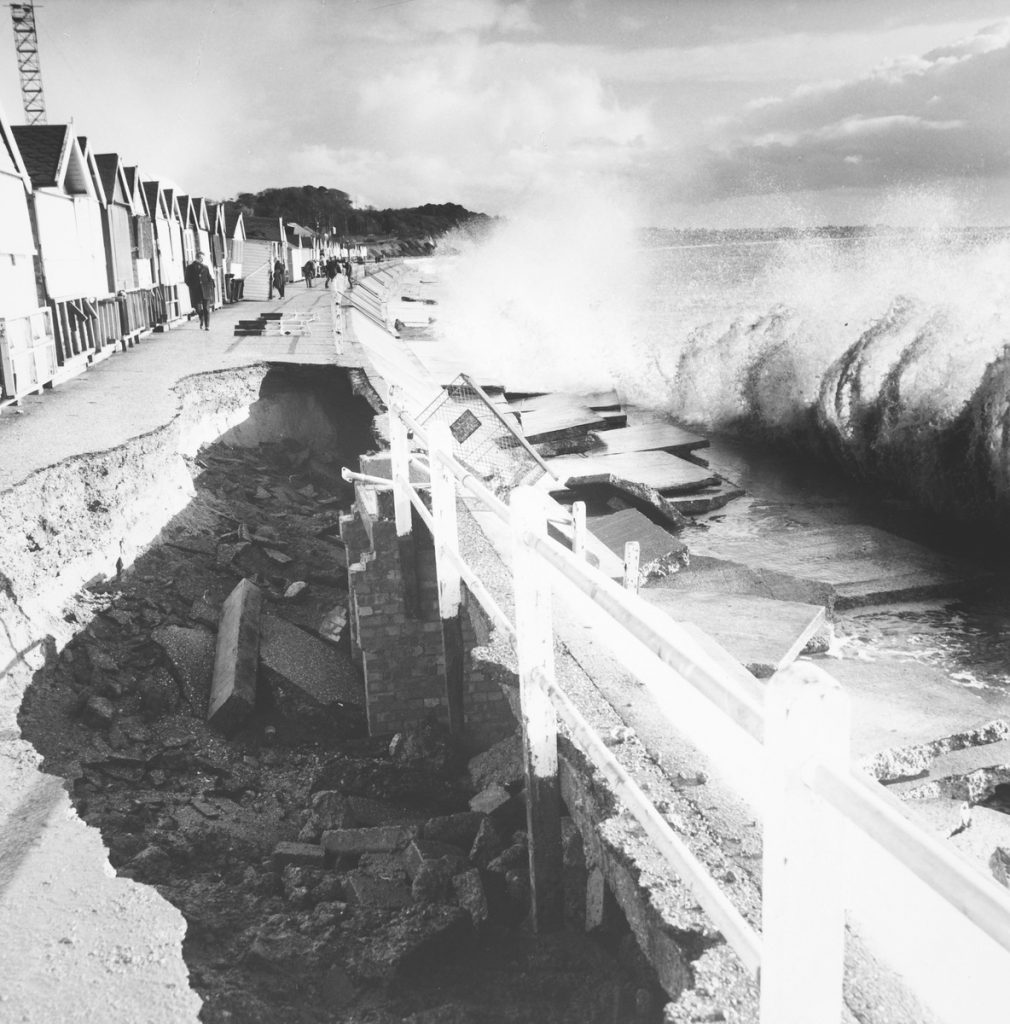 Black and white photograph of rough seas smashing the defences and damaging the promenade, Friars Cliff, Christchurch