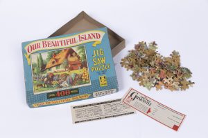 Jigsaw puzzle box featuring country cottage, jigsaw puzzle in a pile, and two leaflets (MERL 2012/283/1-4)