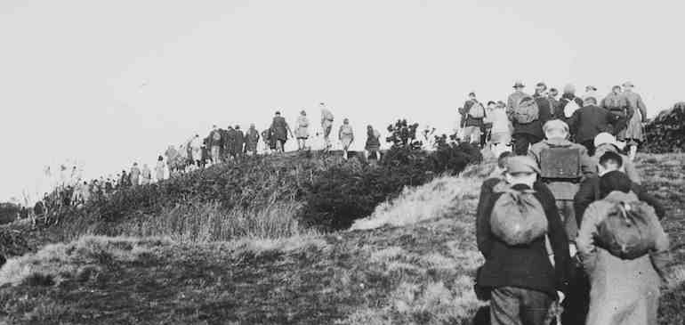 Black and white lantern slide of people walking on a hill