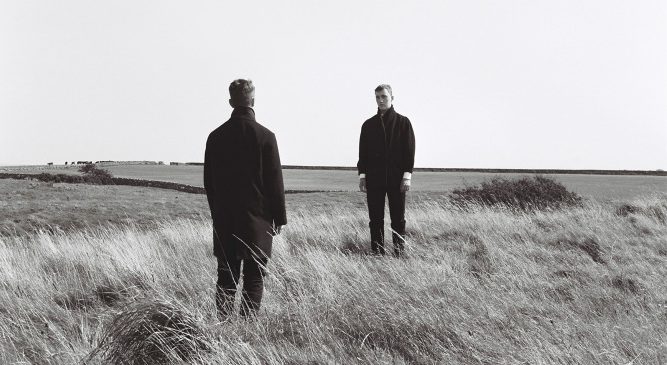 Black and white photograph of two men looking at each other in a landscape setting, by Gemma Dagger.