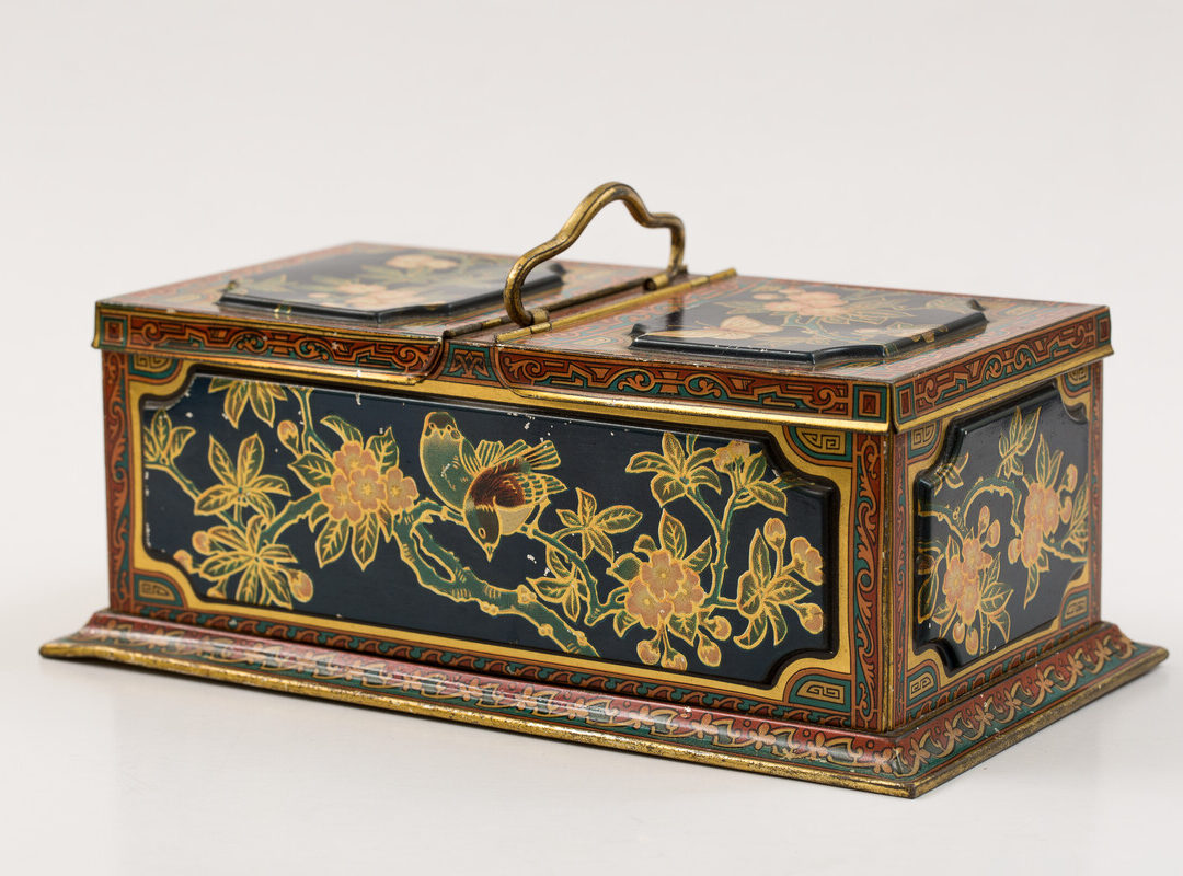 A Christmas floral biscuit tin. This tin has a rectangular shape with two compartments, each with its separate hinged lid. Decorated on all sides with flowers, butterfly, dragonflies and birds. Hinged lifting handle. The biscuits were made by Huntley & Palmers and the tin was made by Huntley, Boorne & Stevens in 1900.