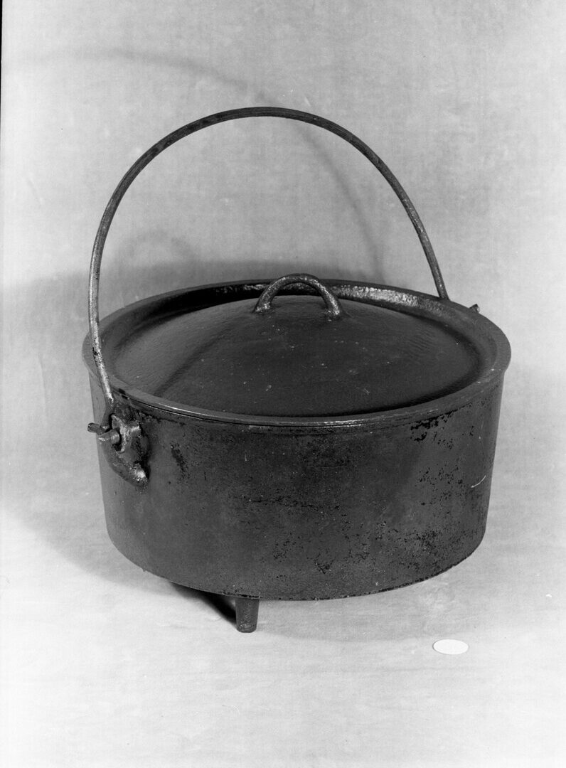 Pot, cooking (object name) This is a heavy cooking pot with a lid, handle, and three short legs, for use in domestic cooking.