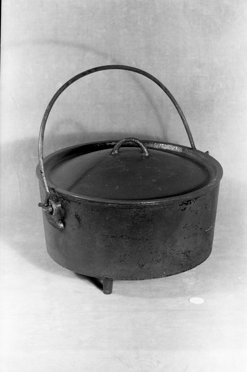 This is a heavy cooking pot with a lid, handle, and three short legs, for use in domestic cooking.