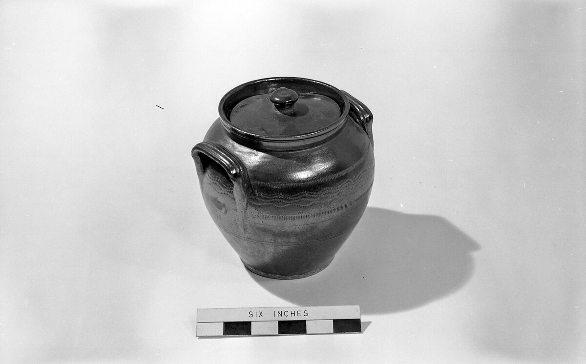 This is a brown stoneware jar and a lid, which was used for storing food.