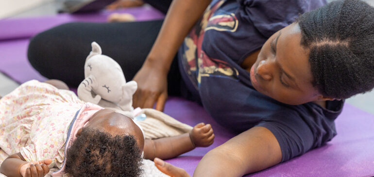 A mum lies next to a baby on a mat as they take part in a Mums and Baby yoga session at The MERL