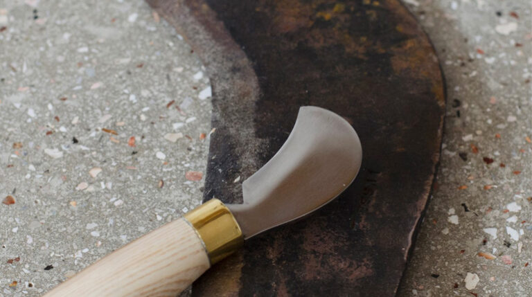 A small bill hook with a wooden handle lying on top of a larger blade