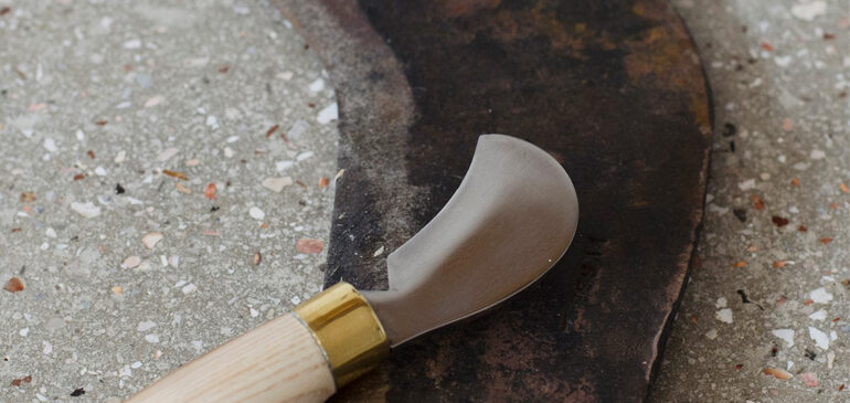 A small bill hook with a wooden handle lying on top of a larger blade