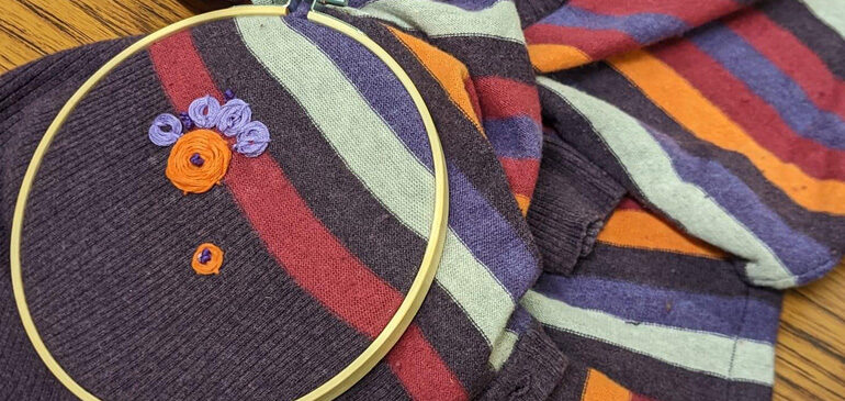 part of a recycled garment in an embroidery hoop with flowers being sewn on