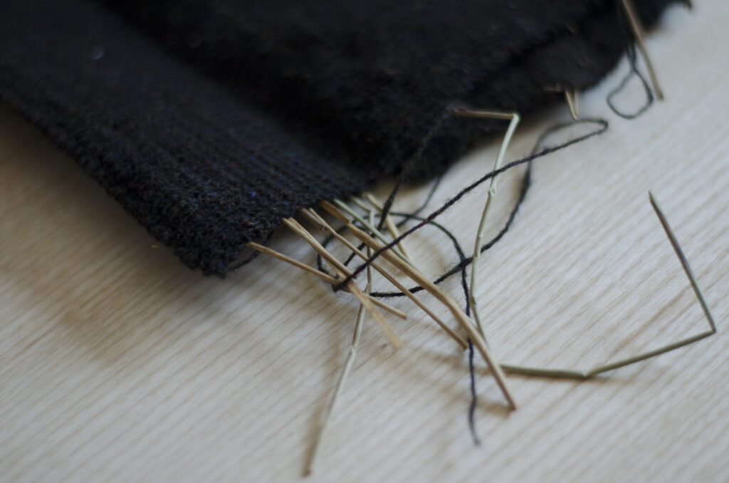 Detail showing water reeds wrapped in machined-knitted dark wool fabric against a table top surface.