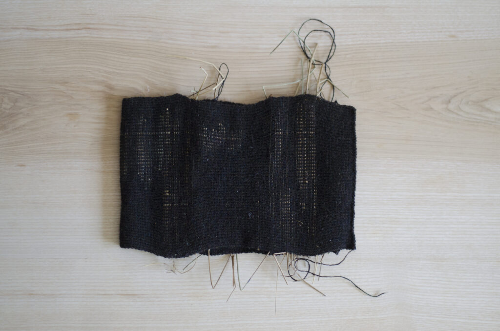 Water reeds wrapped in machined-knitted dark wool fabric against a table top surface.