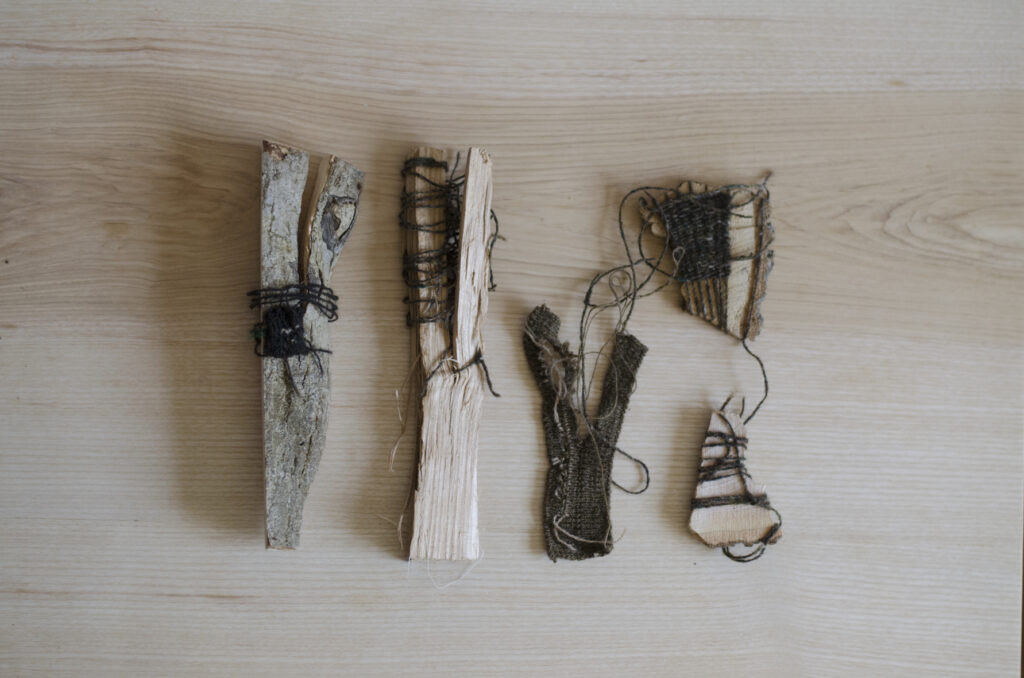 A set of pieces comprising threads of machine-wool bound to green ash on a table top surface.