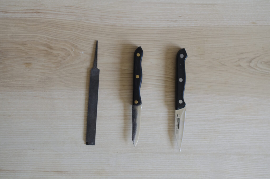 Deconstructed file, handmade paring knife, and the mass-produced knife, all sitting on table top surface