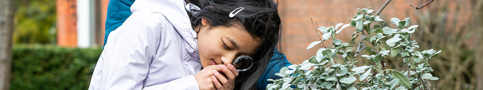 a girl uses a magnifying glass to explore a plant in the MERL garden