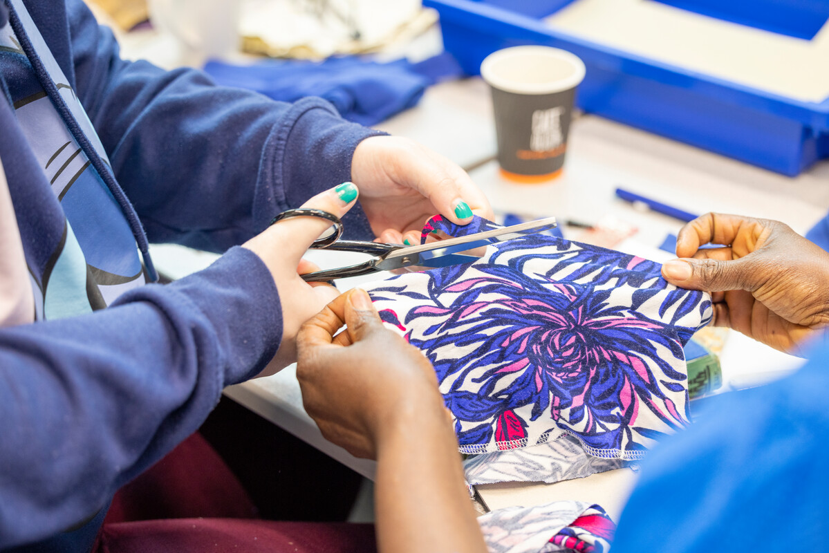 a close up of two people holding a piece of brightly coloured fabric, with one of them cutting into it