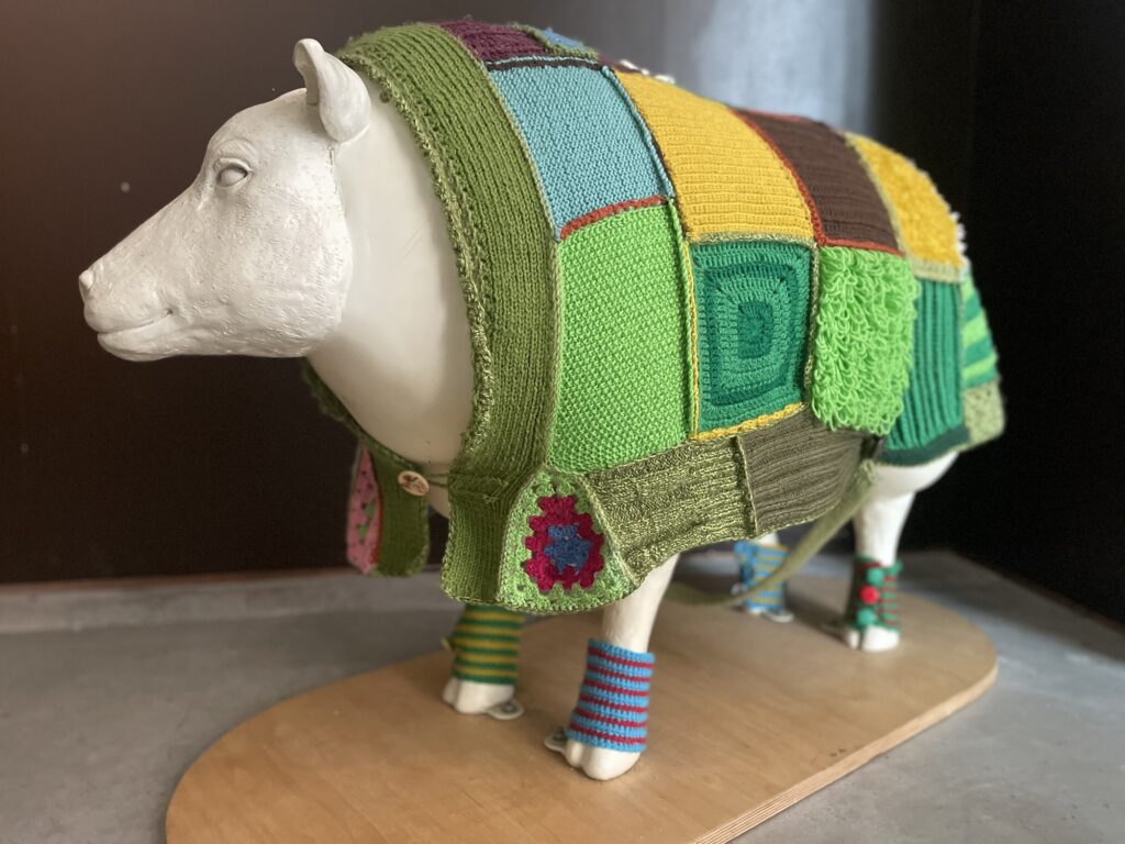 A white plastic sheep wearing a colourful landscape-inspired cardigan