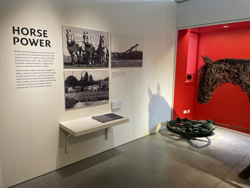 A gallery display entitled 'horse power' featuring a horse engine and a basketwork horse sculpture