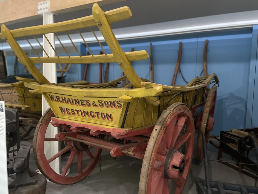 A yellow farm wagon with red wheels on display in a museum gallery