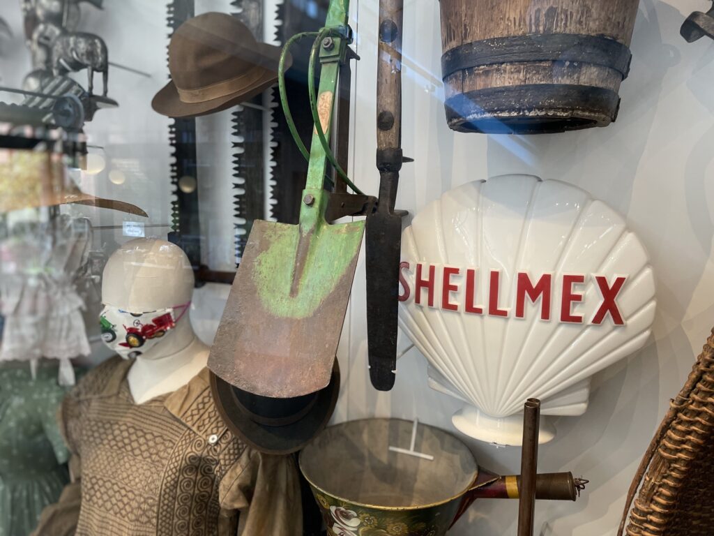 A mixture of cultivation and craft objects with a shellmex petrol pump globe and a mannequin in a smock wearing a facemask