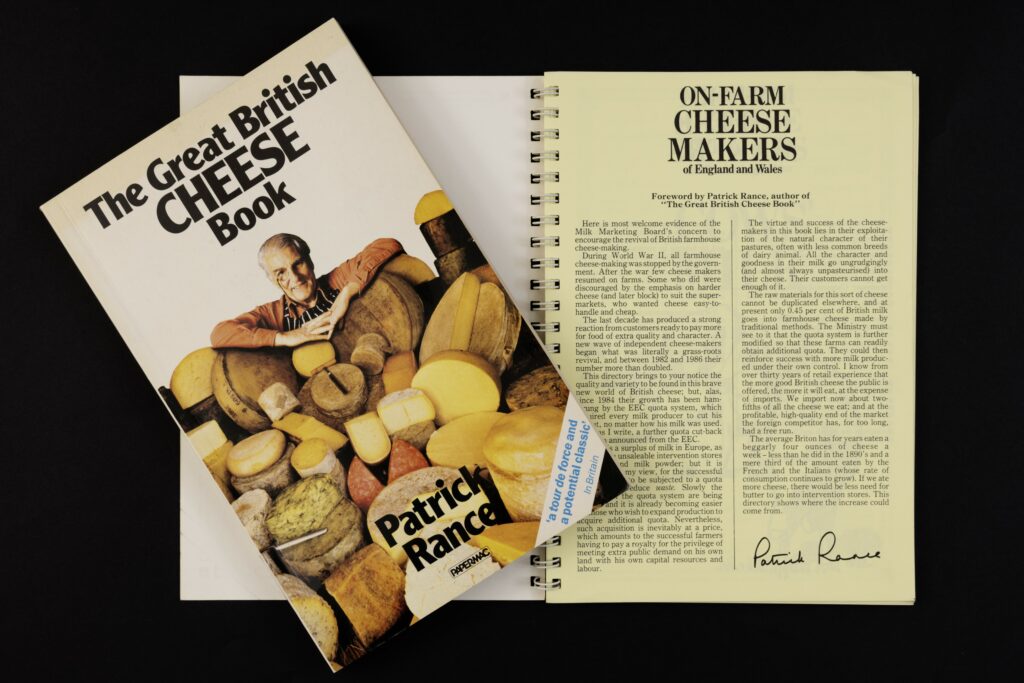 Front cover of a book entitled The Great British cheese book featuring its author, Patrick Rance, among a range of cheese of different shapes and colours. Also a page of text pritned in another bok and signed by Patrick Rance