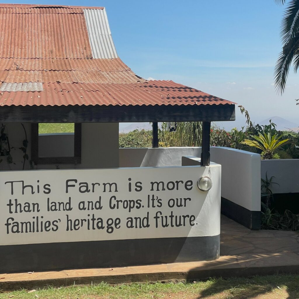 Colour image of Simba Farm Lodge with red roof, white walls, and vegetation and hills in the distance. Words painted on the walls read: 'This Farm is more than land and crops. It's our families' heritage and future.'