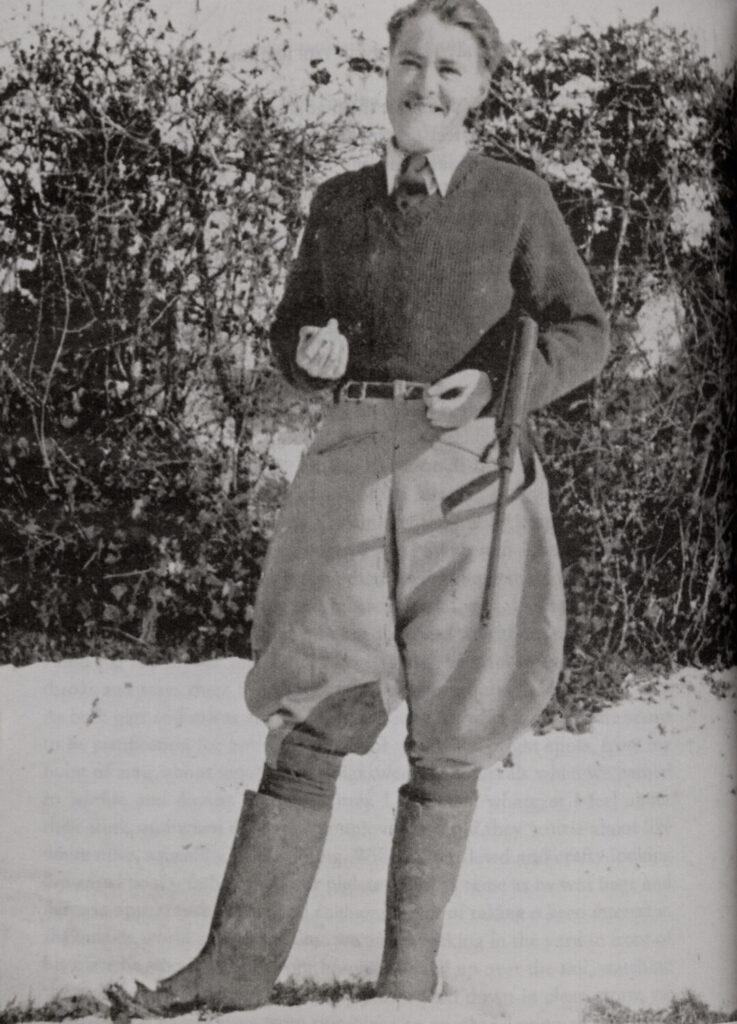 Portrait of Barraud in a jumper, trousers, and boots, holding a gun.