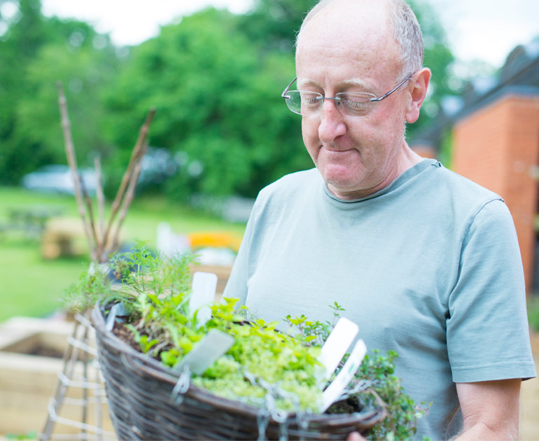 A volunteer in a green shirt holding a hanging basket in the MERL garden.