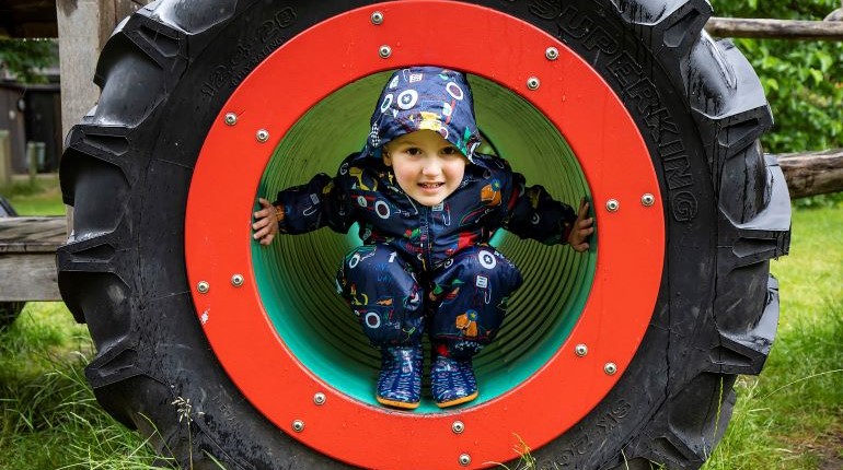 Child in a splash suit sitting in the wheel of the play tractor in the MERL garden