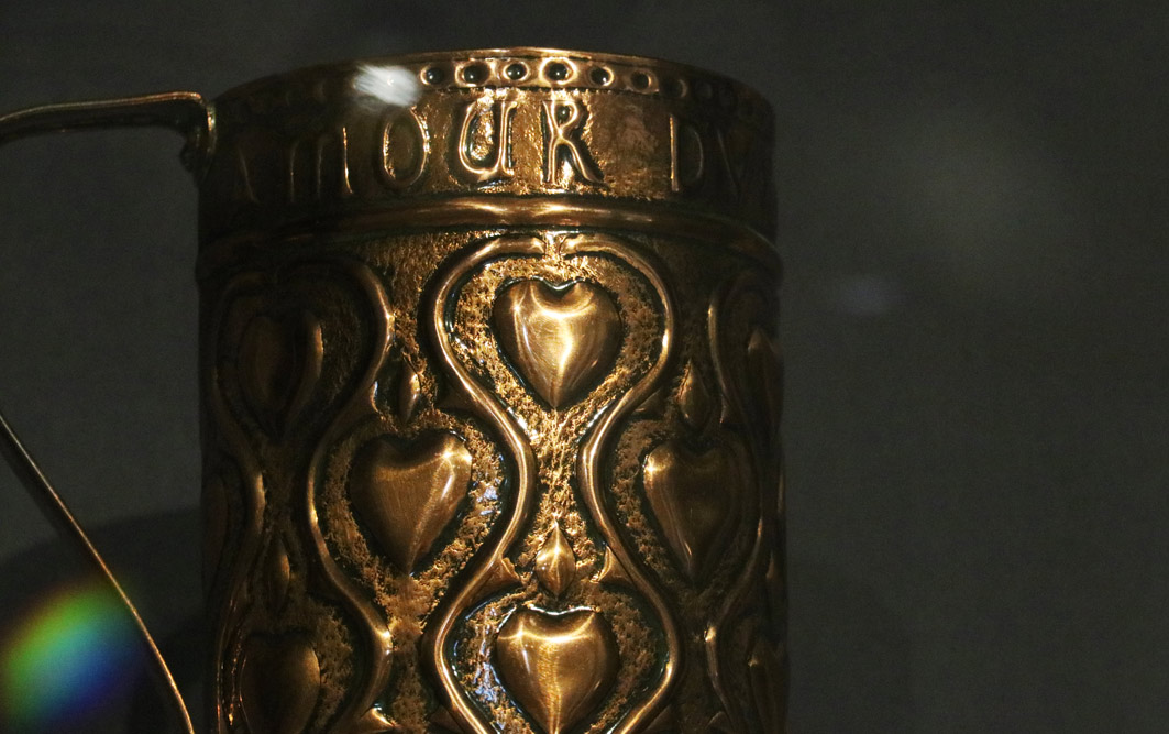 A detail of a copper mug, decorated with hearts.