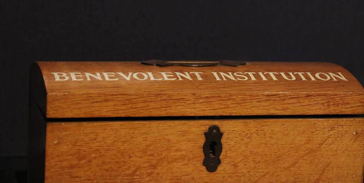 A detail of a wooden box with the words 'Benelovent Institution' painted on it in white.