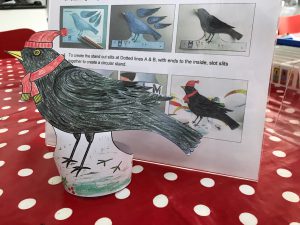 a coloured in paper blackbird on a table in front of step by step picture instructions