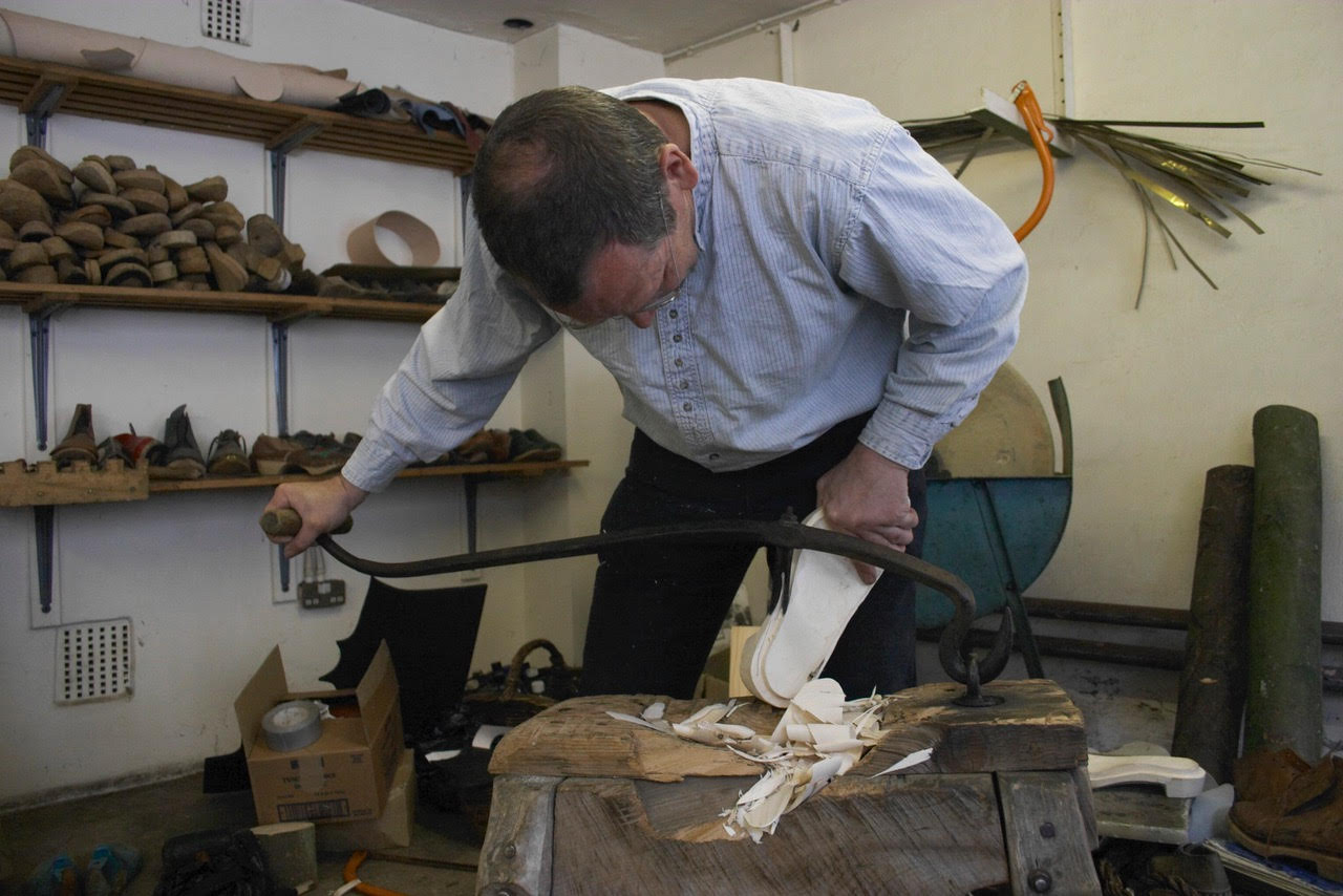 A man in a shirt and jeans, leaning over a wooden clog on a trestle.